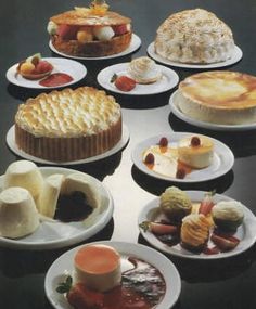 a table topped with lots of different types of cakes and pies on white plates