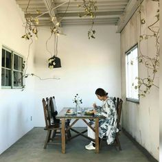 a woman sitting at a table in front of a window with flowers on the table