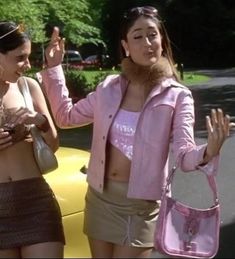 two women standing next to each other in front of a yellow car and one is holding her hand up