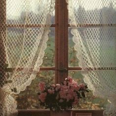 a vase filled with flowers sitting on top of a window sill next to a curtain