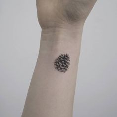 a small pine cone tattoo on the wrist