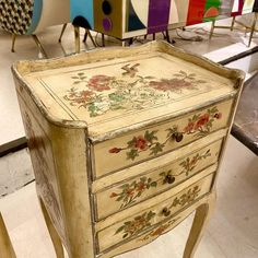 an old chest of drawers with flowers painted on the top and bottom, sitting in a room full of chairs