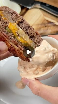 a sandwich being held up in front of a bowl of cream cheese and pickles