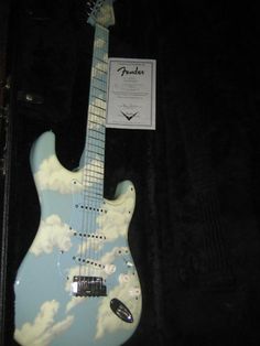 a blue and white guitar with clouds on it's body in a display case