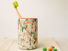 a toothbrush in a cup next to some candies on a towel with a white wall behind it