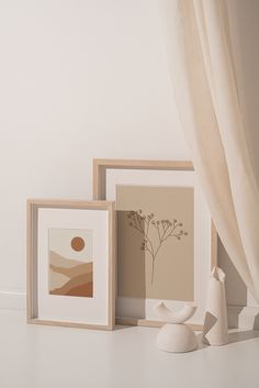 three framed art pieces sitting next to each other on a white counter top with a curtain in the background