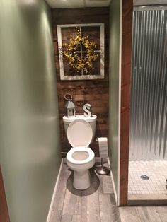 a white toilet sitting inside of a bathroom next to a walk in shower and wooden floors