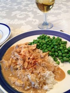 a white plate topped with green peas next to a glass of wine and another plate filled with food