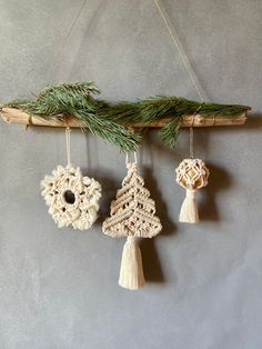 three ornaments hanging from a tree branch with pine needles and tassels on them