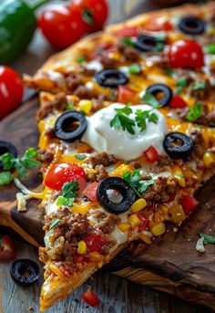 two slices of mexican pizza on a cutting board with tomatoes, black olives and sour cream