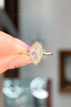 a woman's hand holding an engagement ring in front of her face with the diamond on it