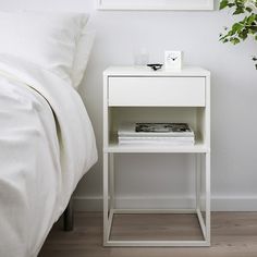 a white bedside table with a clock and magazines on it next to a bed in a bedroom