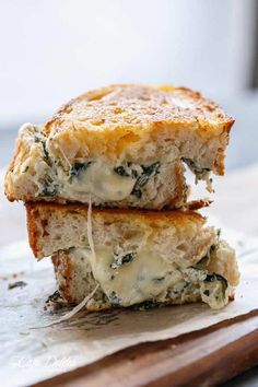 two pieces of bread with cheese and spinach on them sitting on a cutting board