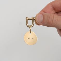 a hand holding a gold keychain with the word nico on it