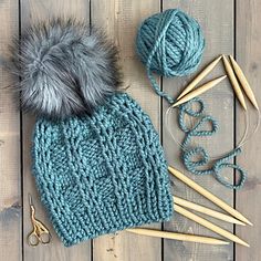 a knitted hat, yarn and knitting needles on a wooden surface with scissors next to it