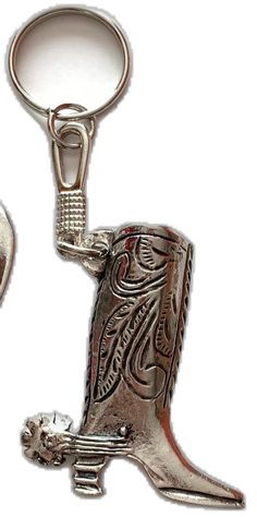 a silver cowboy boot shaped keychain with a skull on the bottom and an ornate design on the side