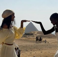 two women in white dresses pointing at each other with pyramids in the back ground