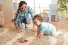 a woman kneeling down next to a baby playing with a toy car on the floor