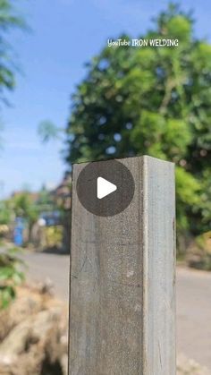 a close up of a wooden post on the side of a road with trees in the background