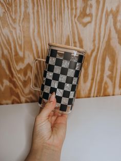 a hand holding a black and white checkered coffee cup on top of a table