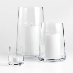 three clear glass vases with white candles in them and one candle on the side