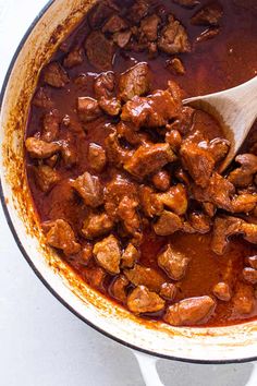 a pot full of meat and sauce with a wooden spoon