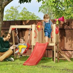 a woman and two children playing in a backyard with a wooden swing set, slide and climbing frame