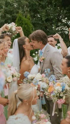 a group of people standing next to each other in front of a wedding cake and flowers