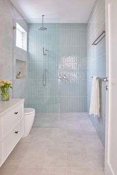 a bathroom with blue tile and white fixtures, including a walk - in shower next to a toilet