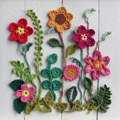 crocheted flowers are arranged on a white wooden surface with green stems and leaves