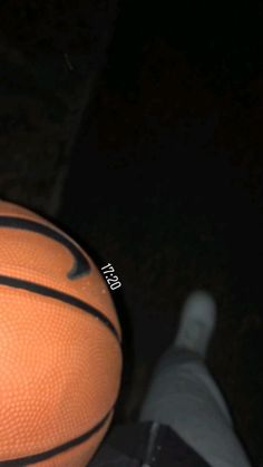 an orange basketball sitting on top of a black floor next to a pair of shoes