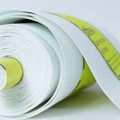 two rolls of white paper are next to each other with yellow tape around them on a white surface