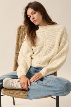 a woman sitting in a chair with her legs crossed wearing jeans and a white sweater