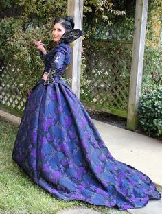 a woman in a blue and purple dress standing on the grass with her hand out