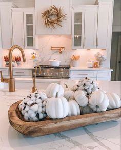 white pumpkins and cotton balls in a wooden tray on a kitchen counter with gold faucet