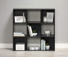 a book shelf with books, vases and other items on it against a gray wall