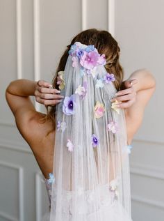 a woman wearing a veil with flowers on it and holding her hair in the air