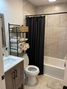 a white toilet sitting next to a bath tub under a bathroom window with black shower curtain