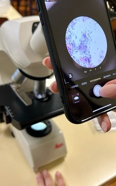 a person holding up a cell phone in front of a microscope