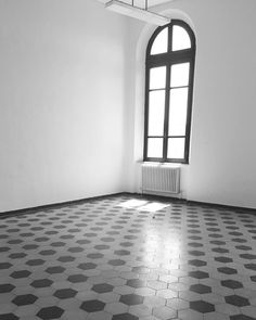 an empty room with black and white tile flooring, large arched window in the corner