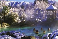 some people are swimming in a pool with snow on the ground and mountains in the background