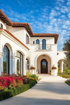 a large white house with lots of flowers in the front yard and landscaping around it