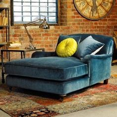 a living room with a blue couch and large clock on the brick wall behind it