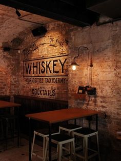 the inside of a bar with wooden tables and stools in front of brick walls