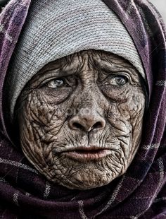 an old woman with wrinkles on her face and scarf around her head is looking at the camera