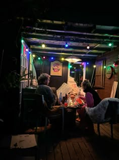 two people sitting at a table in front of a tent with lights on the roof