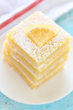 a white plate topped with four pieces of lemon cake covered in powdered sugar and a slice of lemon