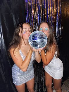 two girls in silver dresses are holding a disco ball