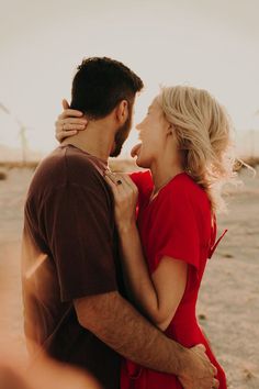 a man and woman standing next to each other in front of wind mills at sunset