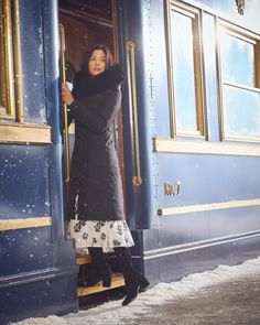 a woman standing in the doorway of a train with her hand on the door handle